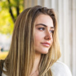 Closeup portrait of beautiful female student leaning on pillar outdoors.